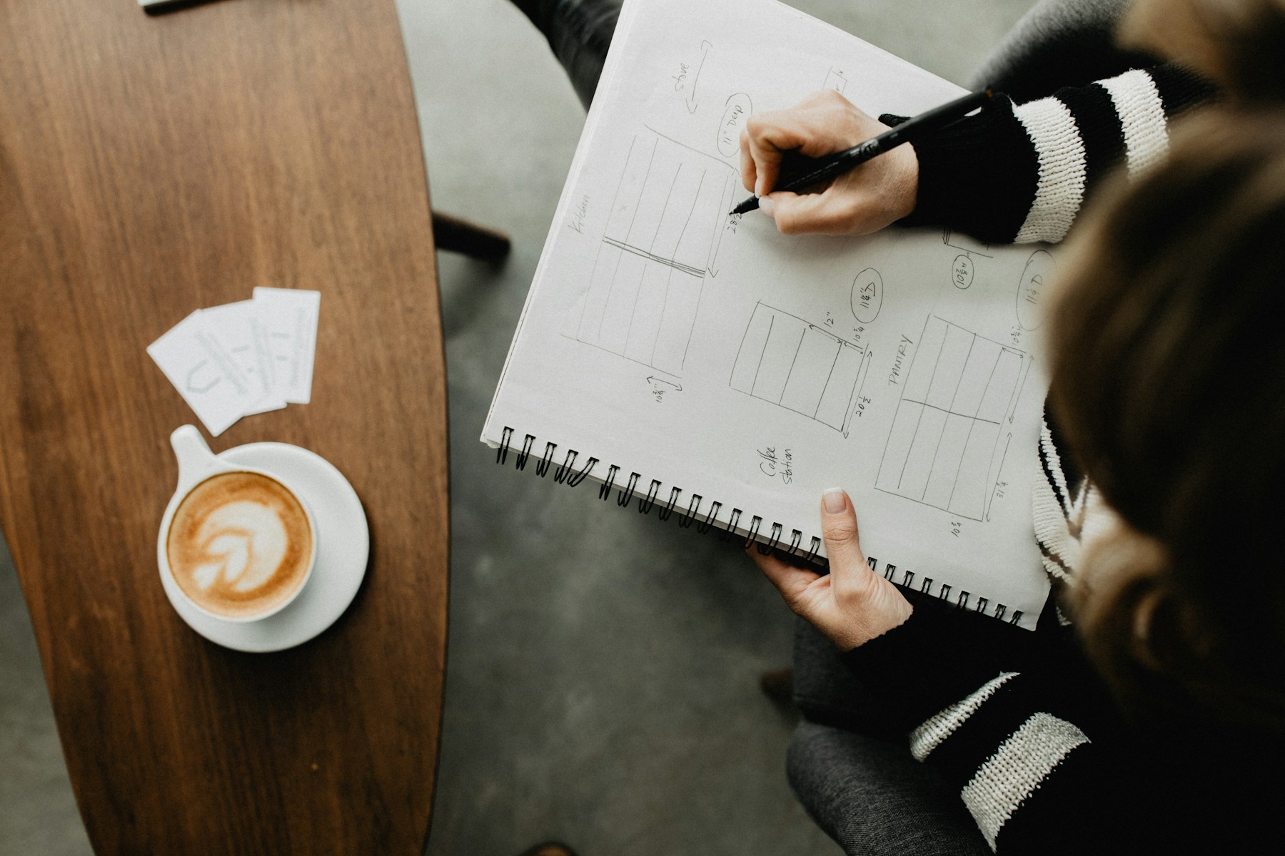 A designer developing ideas in a sketchbook beside a cup of coffee